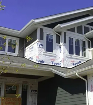 Close-up of residential home under construction with plastic wrap applied for weather protection before siding installation.