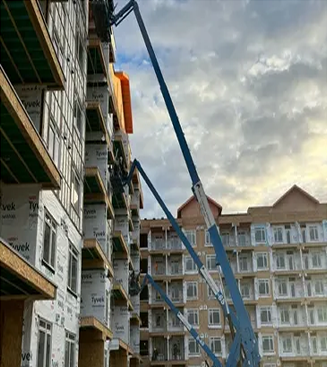 Multi-unit apartment project under construction with cranes on site and protective plastic sheeting over the structure.
